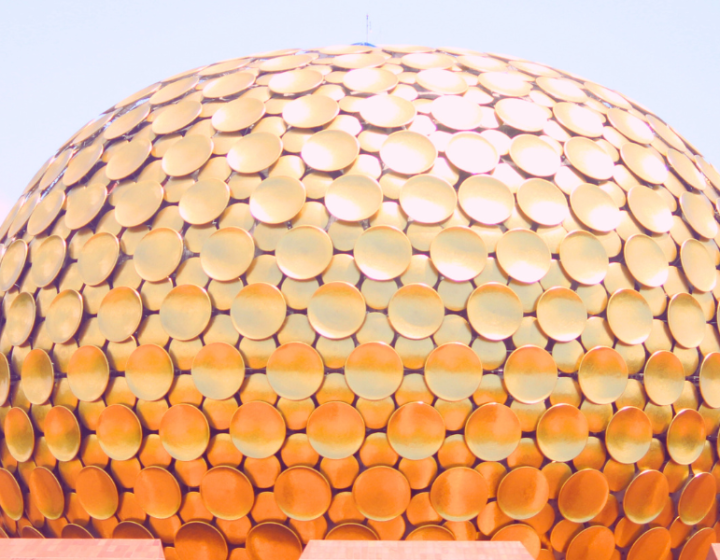 The Matrimandir, a large golden spherical structure, stands prominently against a clear blue sky in Auroville, Pondicherry.